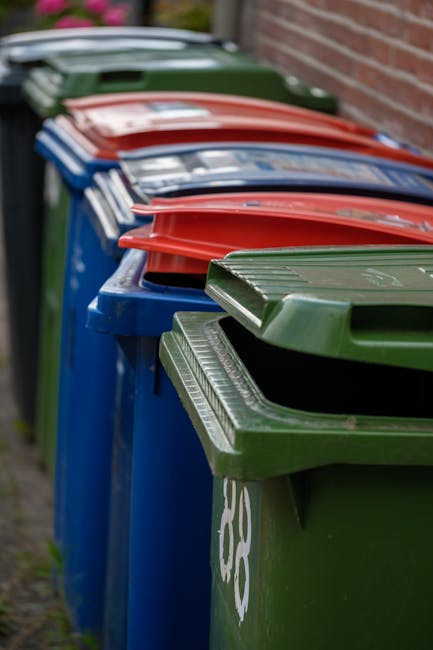 A large pile of black rubbish bags filled with waste is stacked against a tiled wall outdoors. Some bags appear to be partially torn or leaning, with plastic bottles and miscellaneous rubbish visible 